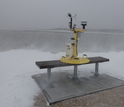 A Weather Pod on a bench next to water and snow