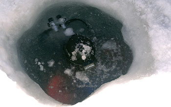 Diver's tank and suit emerge from the thin layer of ice that has formed over the dive hole