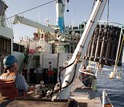 Scientists on ship lower instruments to collected water samples from the ocean.