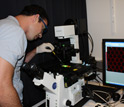 Photo of a scientist pipetting a sample onto a slide on a microscope stage.