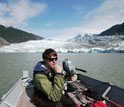 Photo of researcher Eran Hood operating the motor in a boat with Mendenhall Glacier in background.