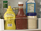 Containers of condiments on a refrigerator shelf