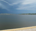 Photo of a body of water with a beach in the foreground and a finger of land in the center.