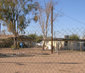 Photo through a fence of a house and sandy lot.