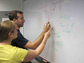 Photo of two researchers working on a problem at a white board.