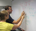 Photo of two researchers working on a problem at a white board.