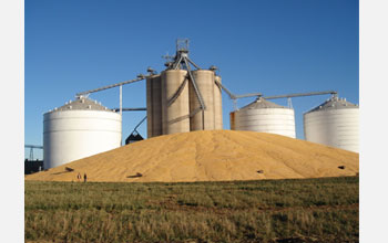 Photo of silos with pile of corn in the foreground.