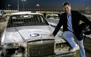 Photo of David Pogue leaning against a car with a NOVA logo on the car's hood.