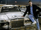Photo of David Pogue leaning against a car with a NOVA logo on the cars hood.