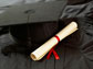 Photo of a degree adjacent to a graduation cap on a black cloth.