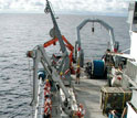 Team of men deploying a core barrel from a research vessel at sea.