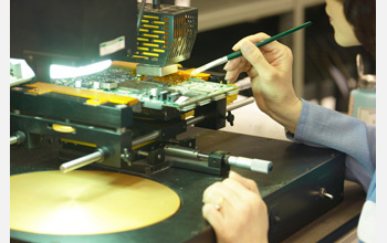 Photo of a worker using a tool on a circuit board.