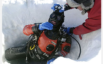 Photo shows a man helping another man prepare to leave the dive hole.