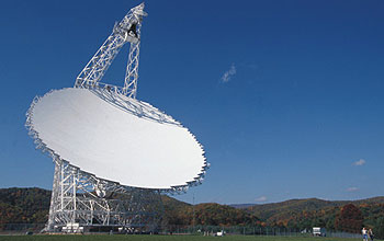 Telescope's broad white dish aims upward at a nearly cloudless sky.