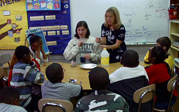 Two adults sign with hands in front of group of students in classroom.