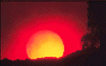 Photo of a red sun on the horizon with silouetted landscape in foreground.
