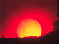 Photo of a red sun on the horizon with silouetted landscape in foreground.