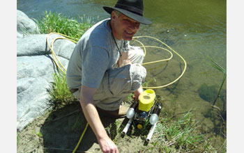 Photo of Hans-Werner Braun deploying a sensor-equipped autonomous underwater vehicle into a stream.