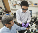 Delaware EPSCoR researcher Juejun Hu holds a sensor chip, while Chaoying Ni looks on.