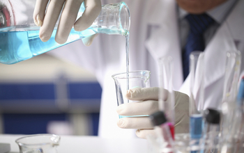 Person in lab coat pouring liquid beaker.