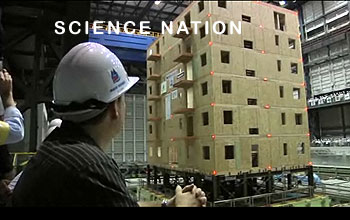 Photo of man in hard hat looking through window at 6-story building on a shake table