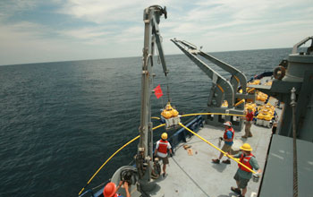 Photo of a crew on a ship using a crane to deploy a receiver in the ocean