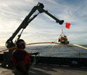 Researcher on a ship pulls a receiver from the ocean using a crane