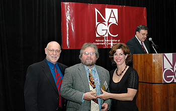 Three people, with one in center holding an award