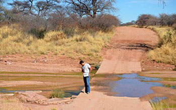 Photo of geologist Kyle Nichols standing next to wet river crossing in Namiba.
