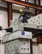 Photo of doctoral student Arash Esmaili checking measurements atop a 110-ft. bridge model.