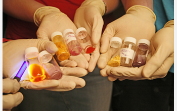 Photo of hands holding conjugated polymers that change color and intensity when excited by light.