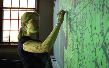 a young woman marking a green screen on the wall.