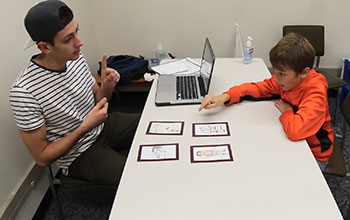 young man across a table from a boy who points to a picture.