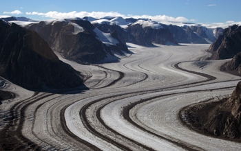 Photo of a glacer with mountains on both sides and trails of rock and soil in the glacier.
