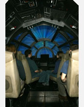 Photo of visitors seated at a full-size replica of the Millennium Falcon cockpit.