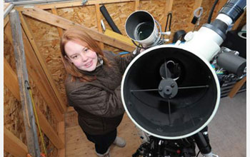 Caroline Moore smiling at work next to a telescope in her home observatory