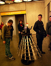 One man smiles at robot while another man eyes it.