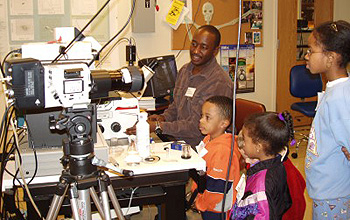 A researcher shows three kids how materials look through the lens of a microscope