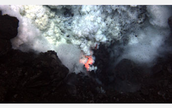 Photo of an explosion of ash and rock at the West Mata Volcano with molten lava glowing below.