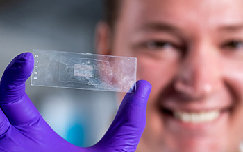 A graduate student displays a microscope slide holding an array of more than 300 microparticles