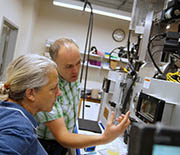 Matthew White and a visiting researcher discuss the features of the dual-vacuum-chamber solar cell fabrication facility at the University of Vermont.