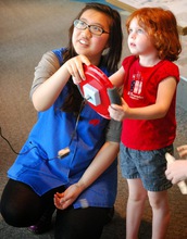 A volunteer at the Science Museum of Minnesota helps a young girl play a driving simulation.