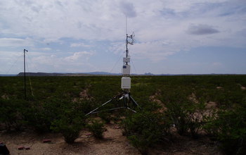 A tower placed on desert ground, with mountains in the background.