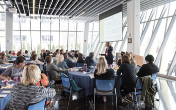 Conference room at Northeastern Illinois University filled with researchers sitting at tables listening to a lecture