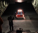 An ambulance moving towards the inside fo a military plane; an individual is directing the ambulance