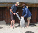 Photo of two researchers putting beach sand from a coring device into a bag.