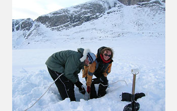 Photo shows 2 people collecting sediment core from a lake on Baffin Island.