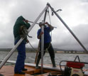 Photo of Curt Stager and Brian Chase collecting a sediment core with storm clouds overhead.