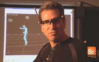 Photo of man in motion capture suit with virtual version on the monitor behind him