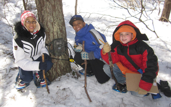 Three young ecology students with a "camera trap" in the woods.